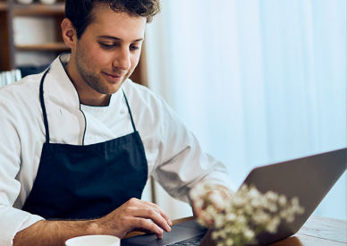 Junger Mann sitzt in seinem Cafe mit seinem Laptop und einer Tasse Kaffee 