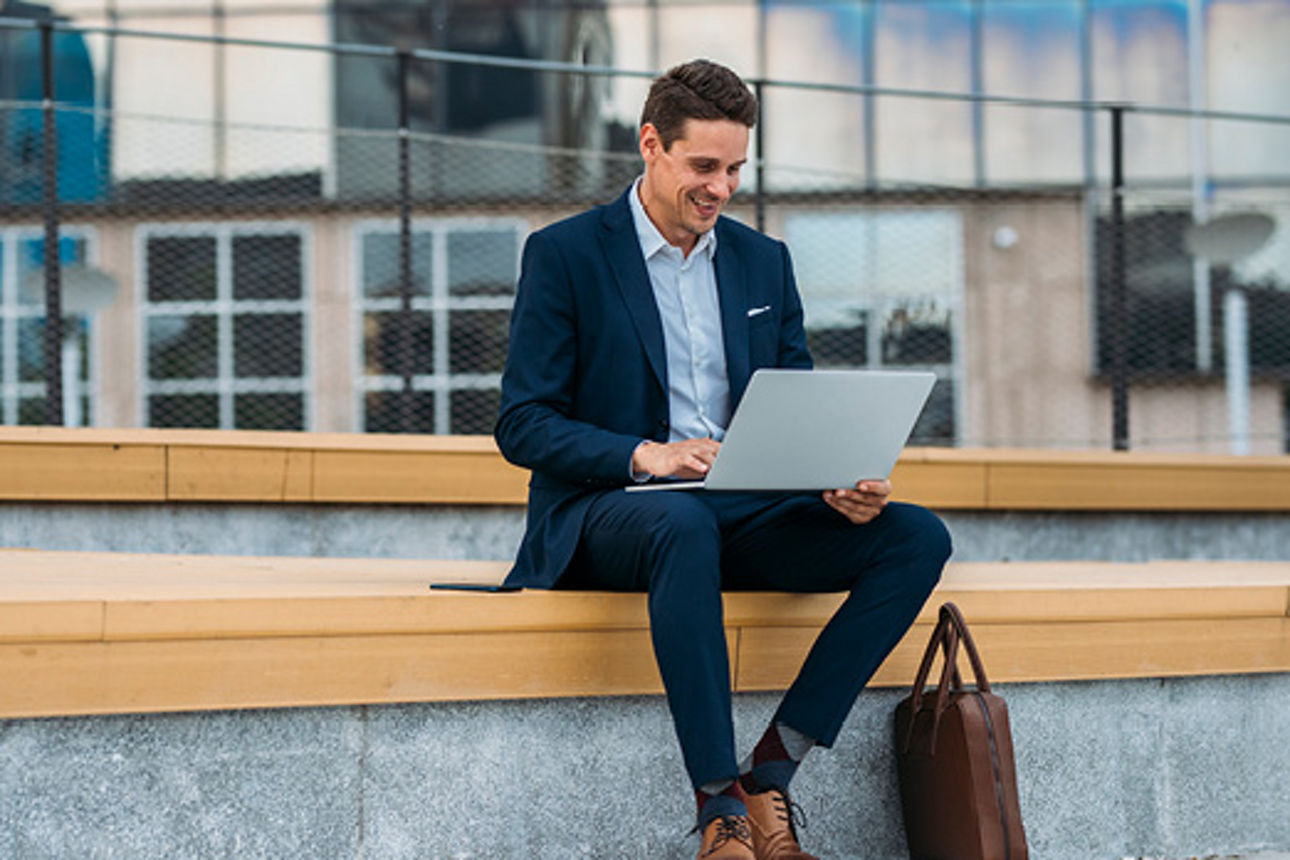 Mann mit Anzug sitzt auf einer Bank mit Laptop