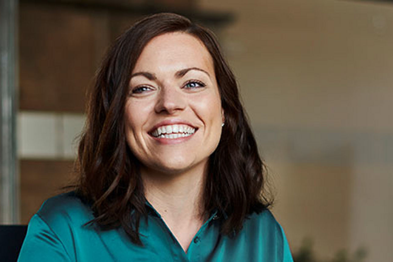 Eine Frau mit langen dunklen Haaren lächelt breit in die Kamera.