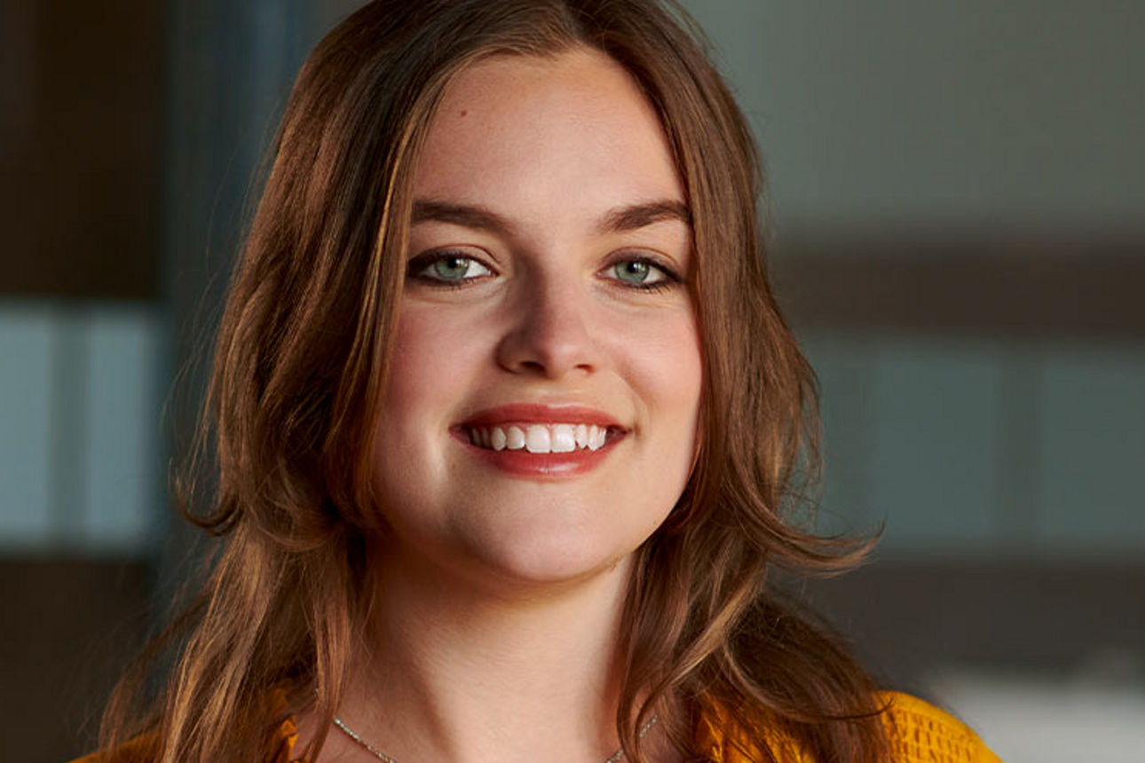 Eine junge Frau in Abschlussmütze und Talar lächelt strahlend in die Kamera.