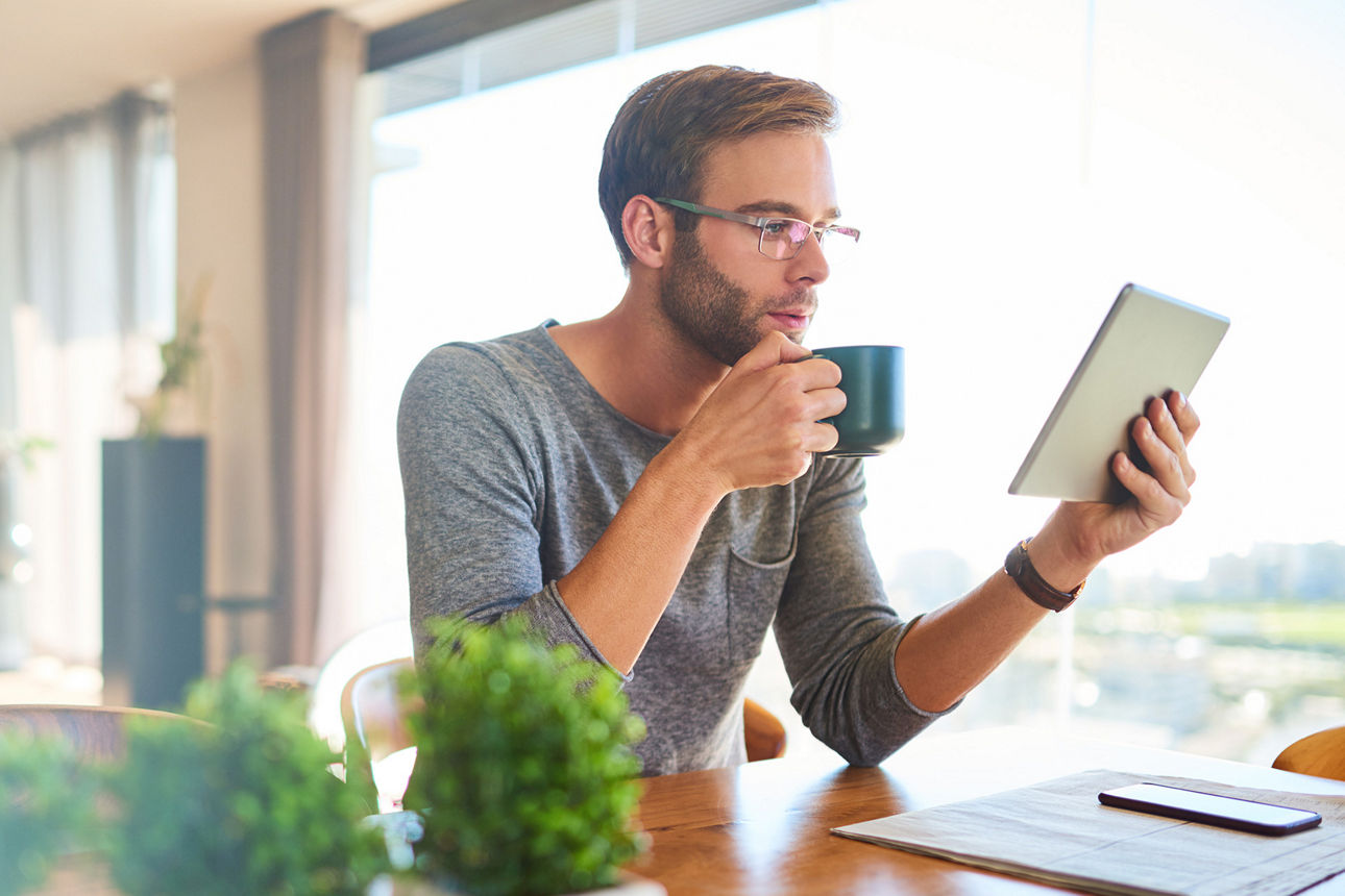 Junger Mann trinkt Kaffee und schaut auf sein Tablet