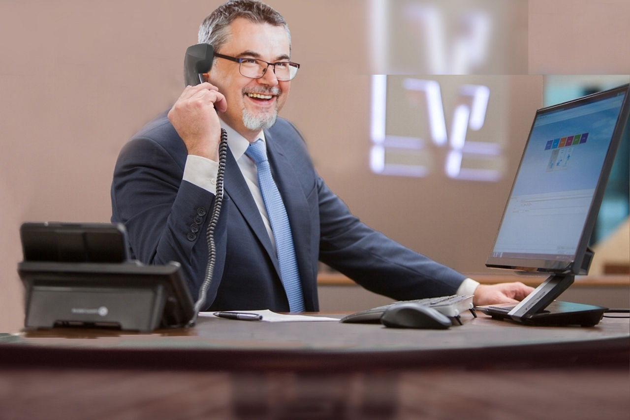 Mann sitzt am Schreibtisch mit Bildschirm und Telefon