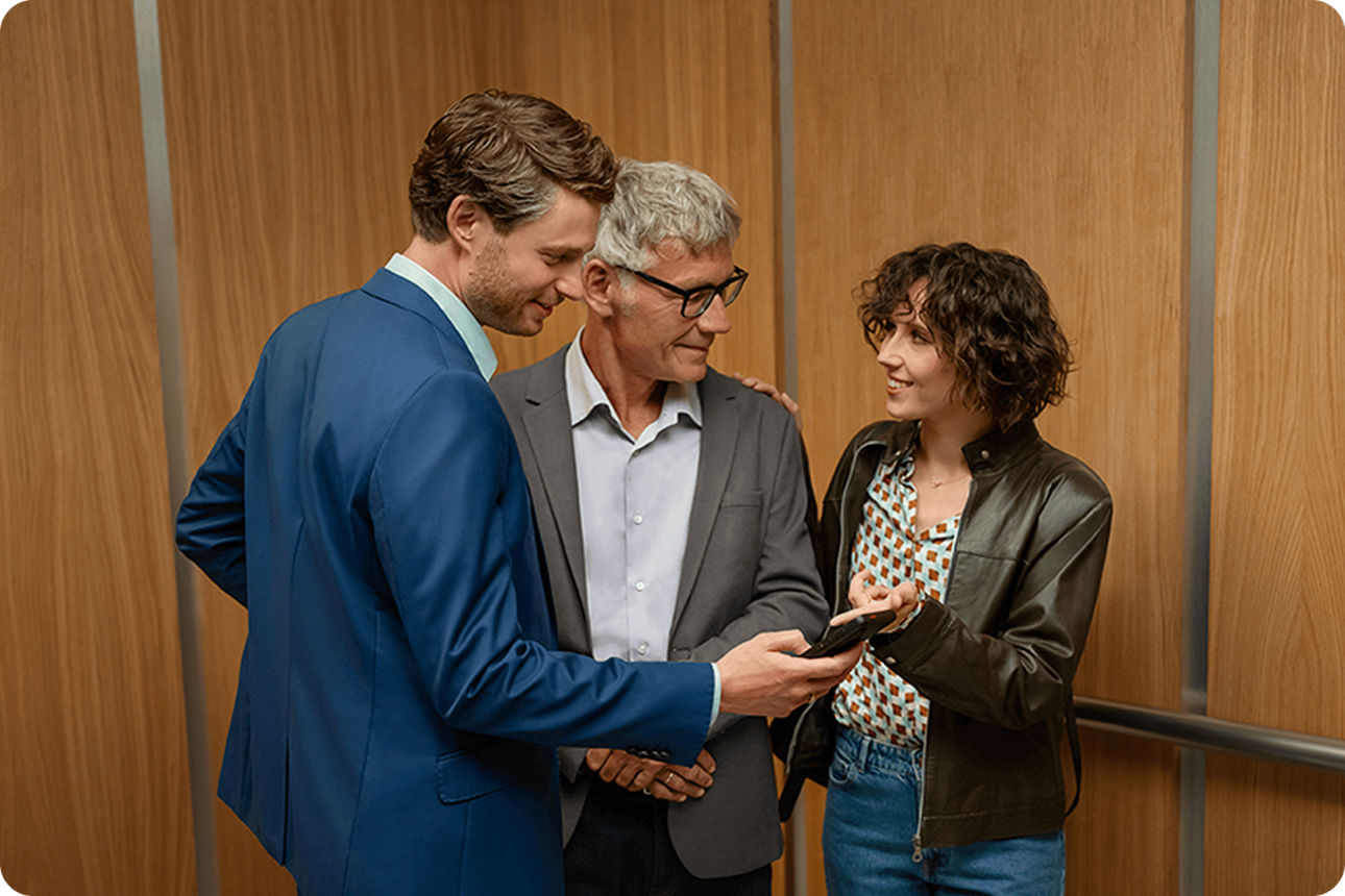 Zwei Männer und eine Frau stehen zusammen und schauen auf ein Handy