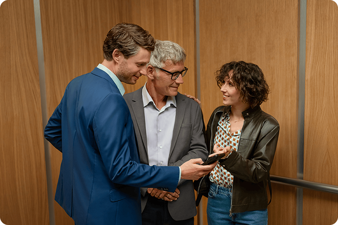 Zwei Männer und eine Frau stehen zusammen und schauen auf ein Handy