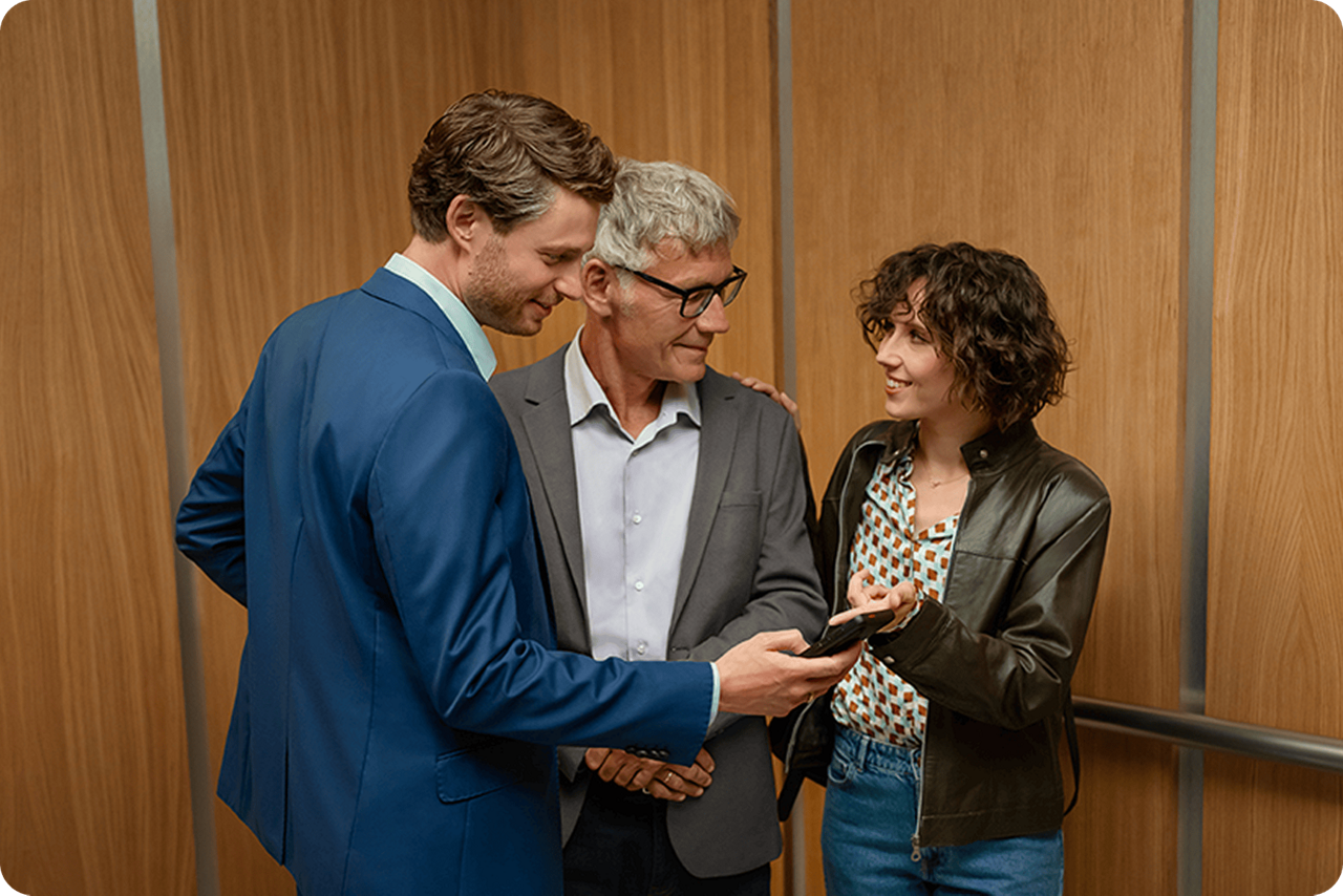 Zwei Männer und eine Frau stehen zusammen und schauen auf ein Handy