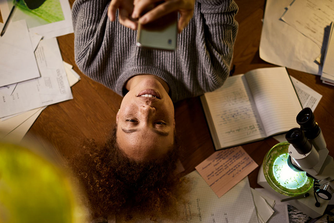 Junge Frau liegt auf dem Fußboden und schaut aufs Handy