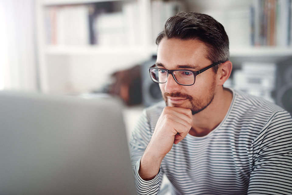Ein Mann mit Brille sitzt vor seinem Laptop und denkt nach