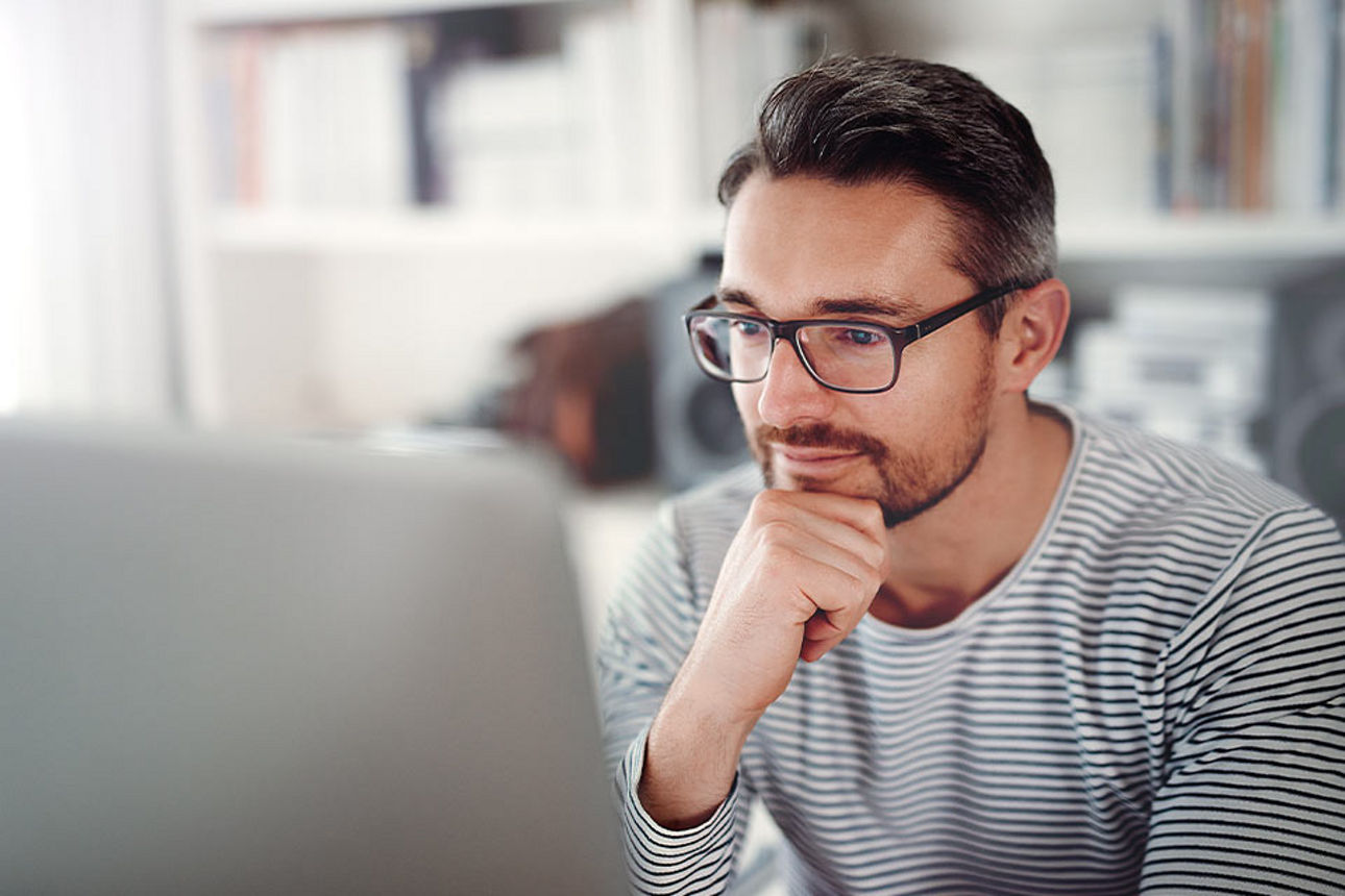 Mann mit Brille sitzt freundlich nachdenklich am Laptop