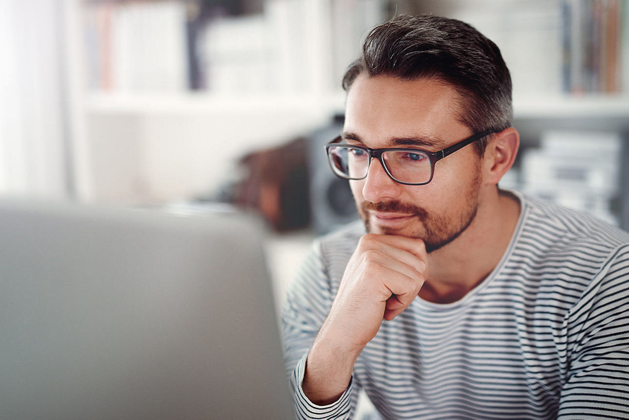 Mann mit Brille sitz vor einen Laptop und hält mit der Hand sein Kinn