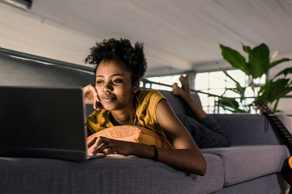Frau liegt auf Sofa und schaut auf ihren Laptop