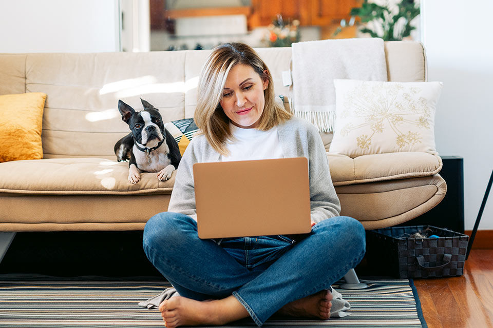 Junge Frau sitzt vor dem Sofa und blickt auf einen Laptop
