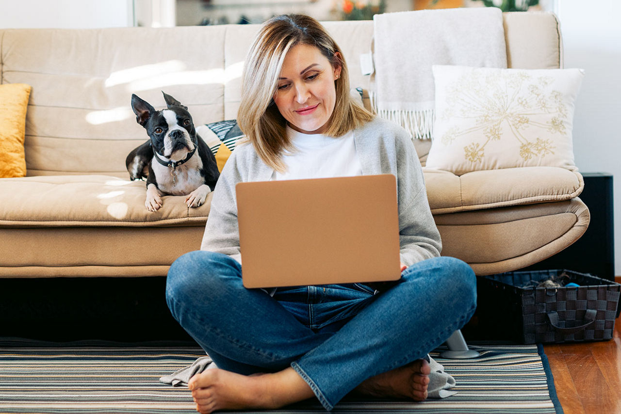 Frau sitzt auf dem Teppich und schaut auf ihren Laptop
