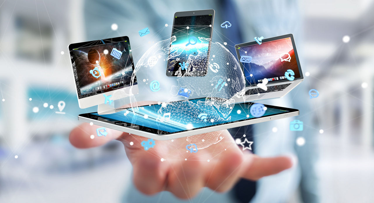 Über einer ausgestreckten Hand eines Mannes mit Krawatte schweben ein Tablet, ein Handy, ein Laptop und ein Computer sowie grafische Icons und die Weltkugel
