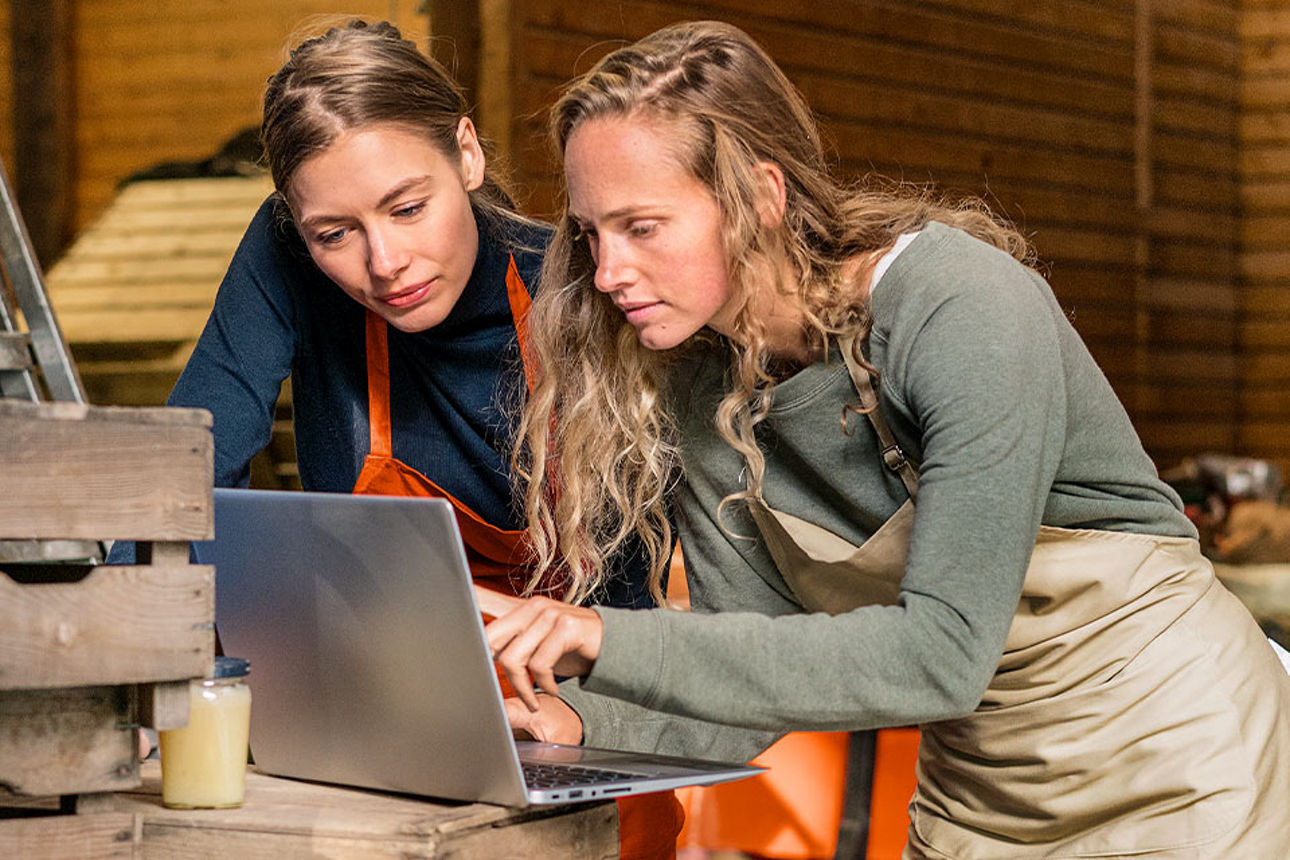 Zwei junge Frauen stehen in einer Werkstatt und schauen gemeinsam auf ein Notebook