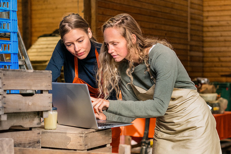 Zwei Damen in Arbeitskleidung benutzen einen Laptop