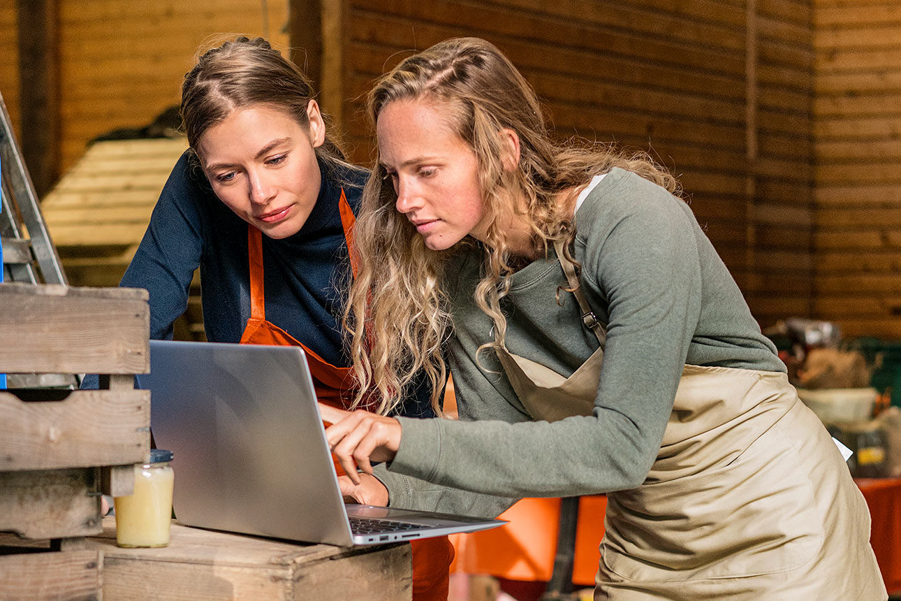 Zwei junge Frauen stehen in einer Werkstatt und schauen gemeinsam auf ein Notebook