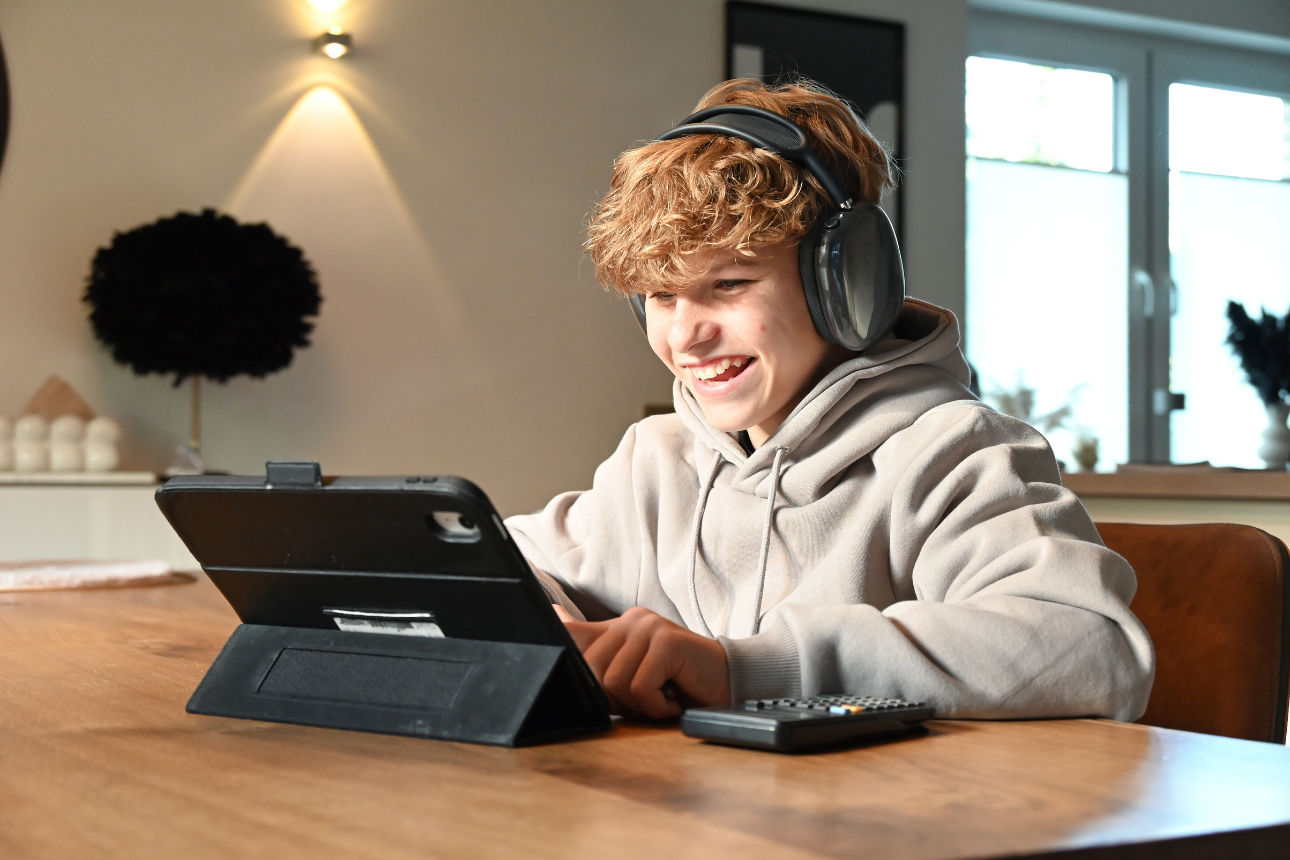 Eine Person sitzt mit großen Kopfhörern an einem Tisch und arbeitet konzentriert an einem Tablet.