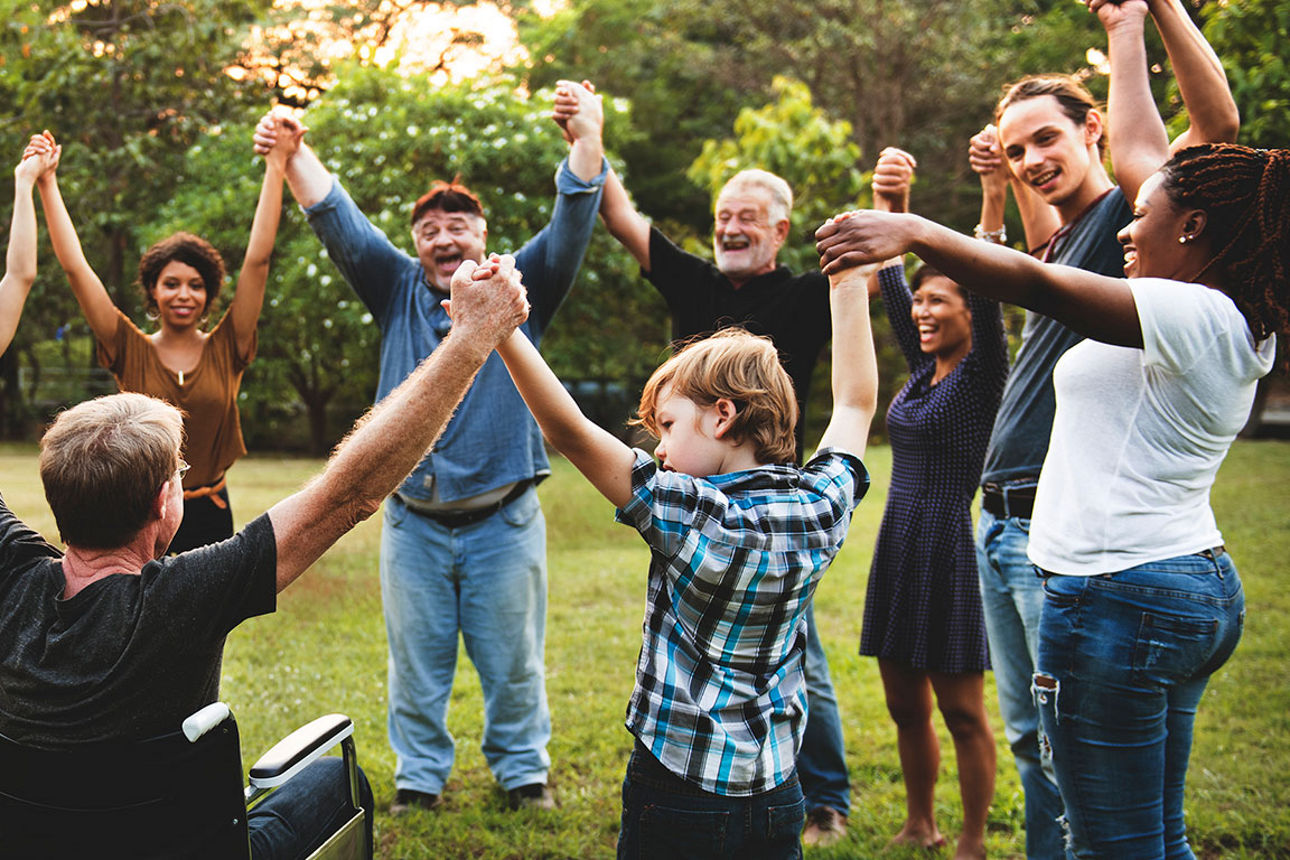 Gruppe von Menschen steht im Kreis im Park, hält sich an den Händen und jubelt gemeinsam.