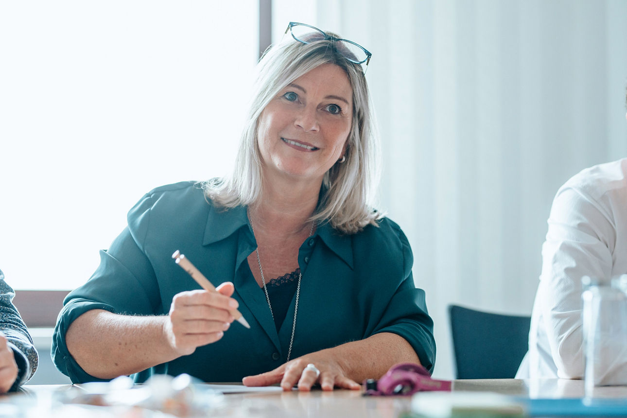 Eine Frau sitzt aufmerksam an einem Besprechungstisch und macht sich Notizen.