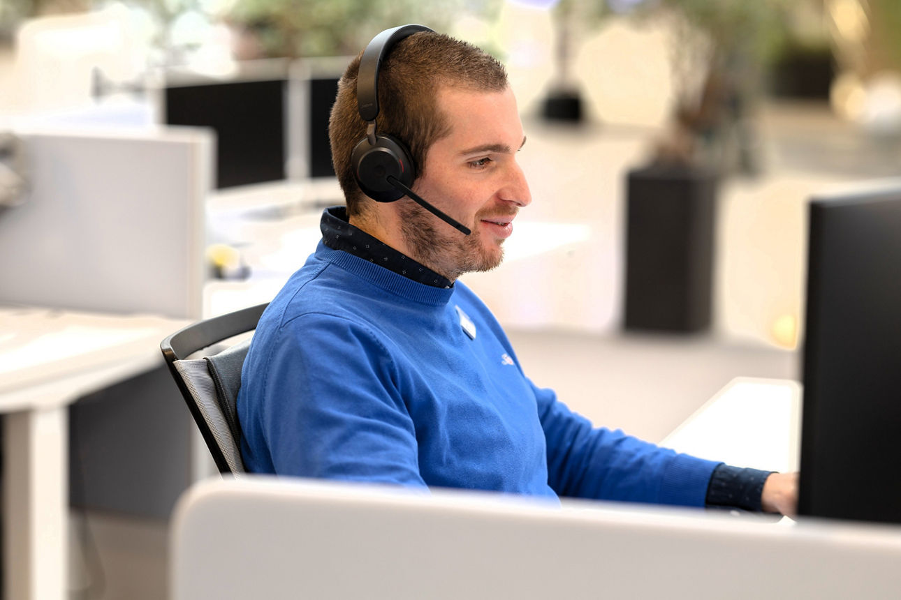 Eine männliche Person sitzt an einem Arbeitsplatz in einem modernen Büro und trägt ein Headset. 