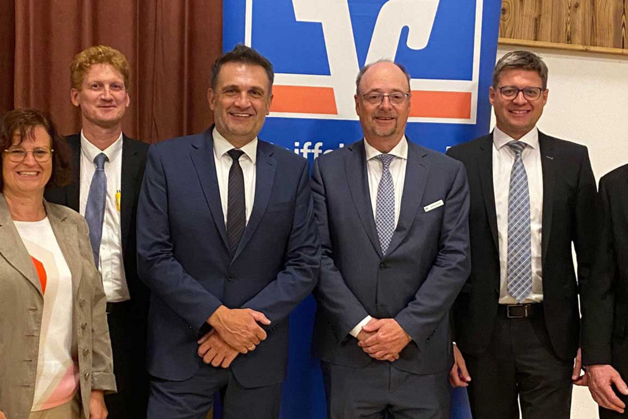Eine Gruppe von sieben Personen in festlicher und Business-Kleidung posiert für ein Foto vor einem blauen Banner der Volksban