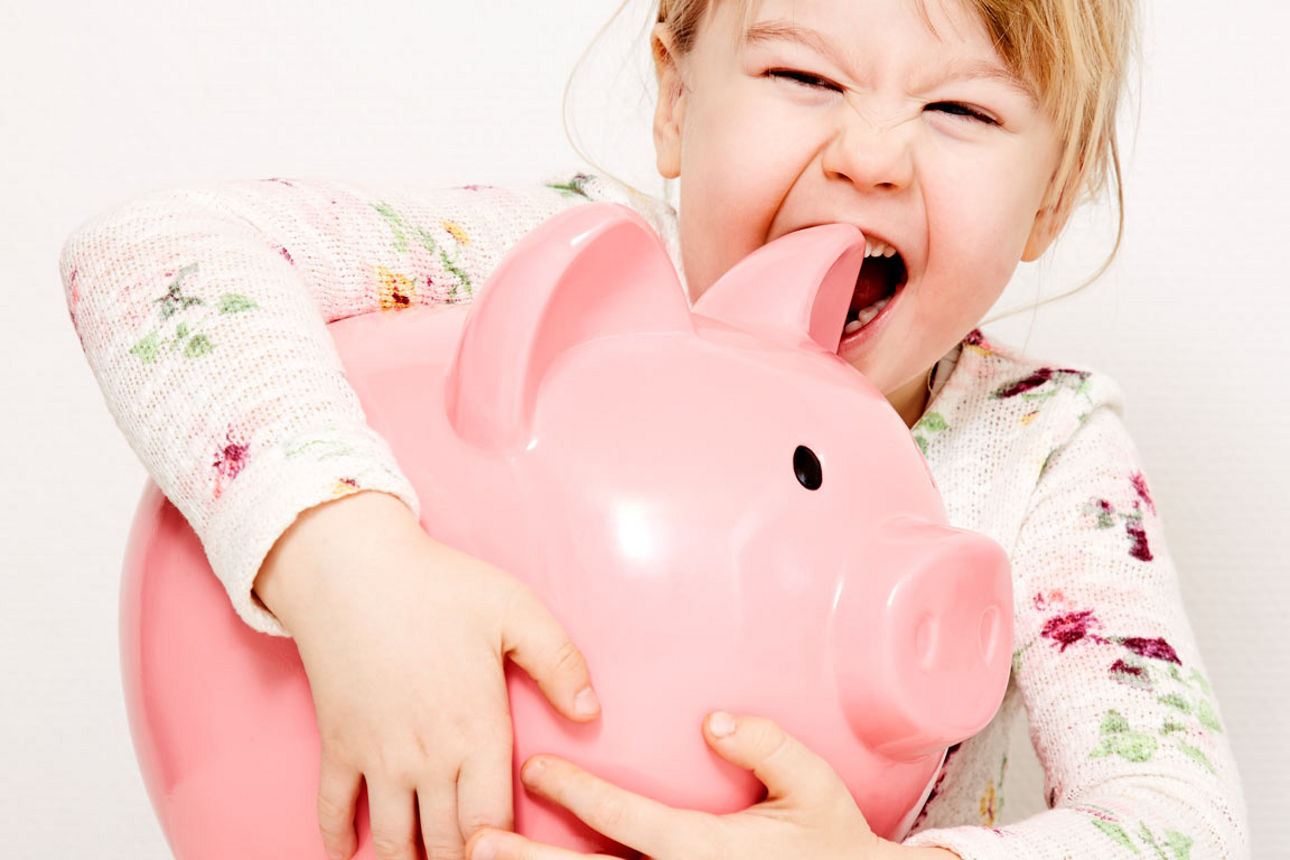 Ein kleines Mädchen umarmt fröhlich ein großes rosa Sparschwein und beißt spielerisch hinein.