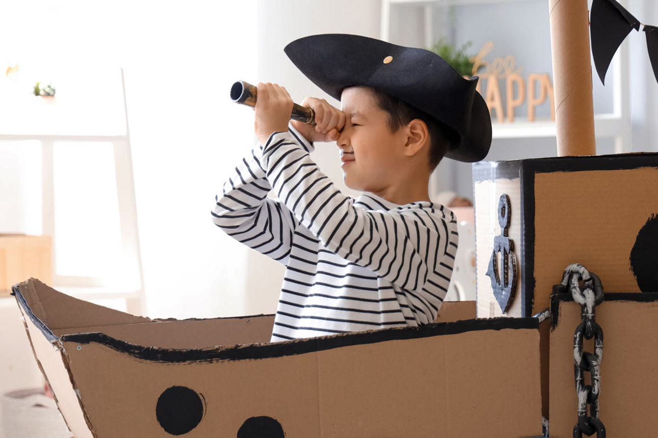 Kind spielt als Pirat in einem Pappboot mit Fernrohr – ein fantasievolles Motiv für Abenteuer, Kreativität und spielerisches 