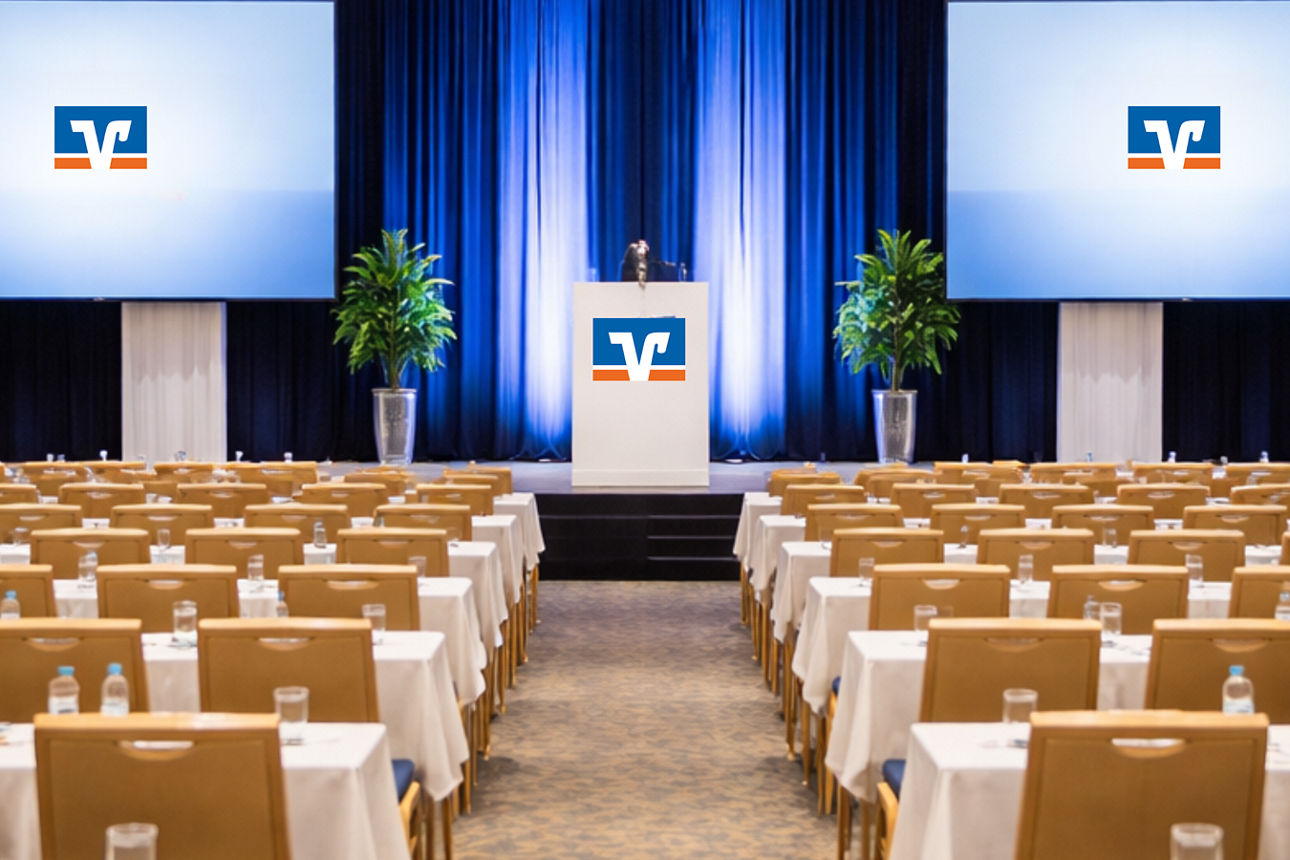 Ein Saal mit Tischen und Stühlen sowie einer Bühne mit dem Volksbank-Logo. 