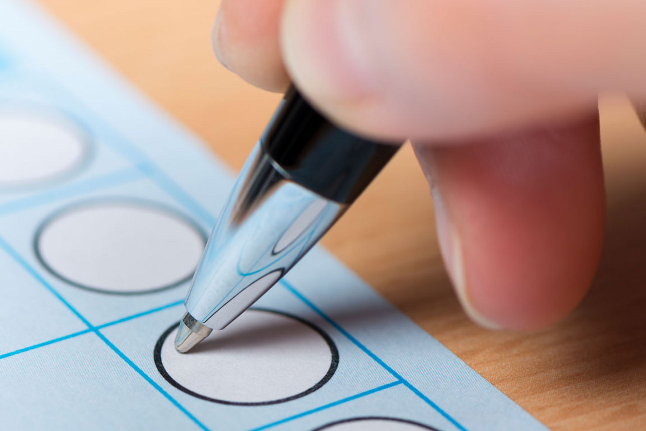 Eine Hand setzt mit einem Stift ein Kreuz in ein Auswahlfeld auf einem Formular.