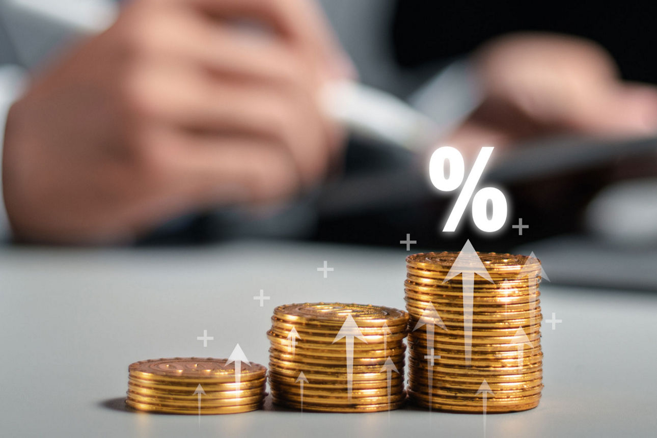 Gestapelte Münzen mit Prozentzeichen und Pfeil nach oben als Symbol für Wachstum und Zinsen.