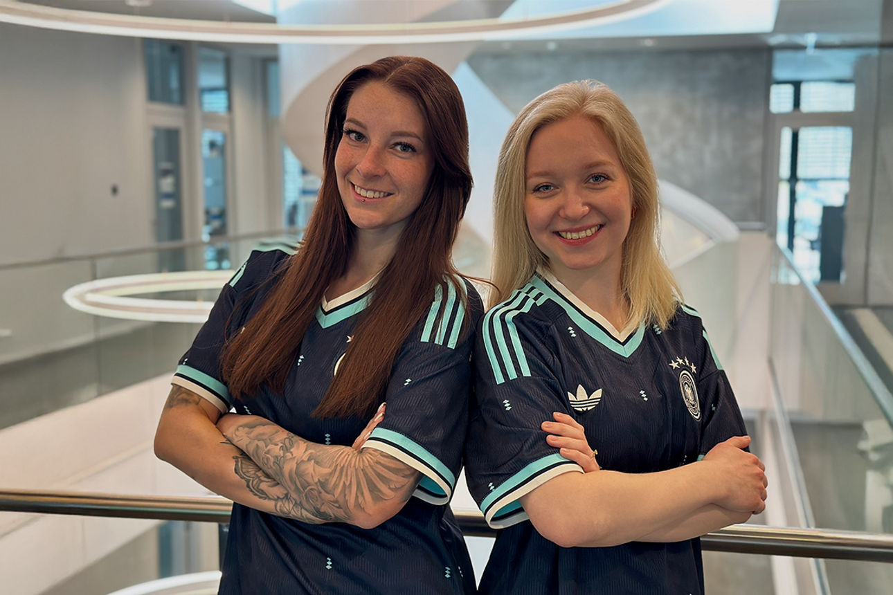 Zwei Frauen stehen Rücken an Rücken im aktuellen DFB-Trikot.