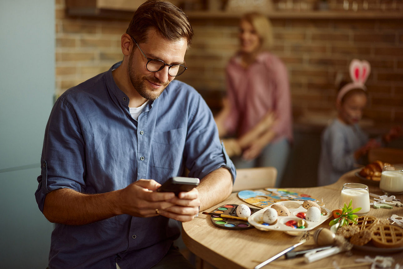 Mann sitzt mit der Familie am Ostertisch und schaut auf sein Handy