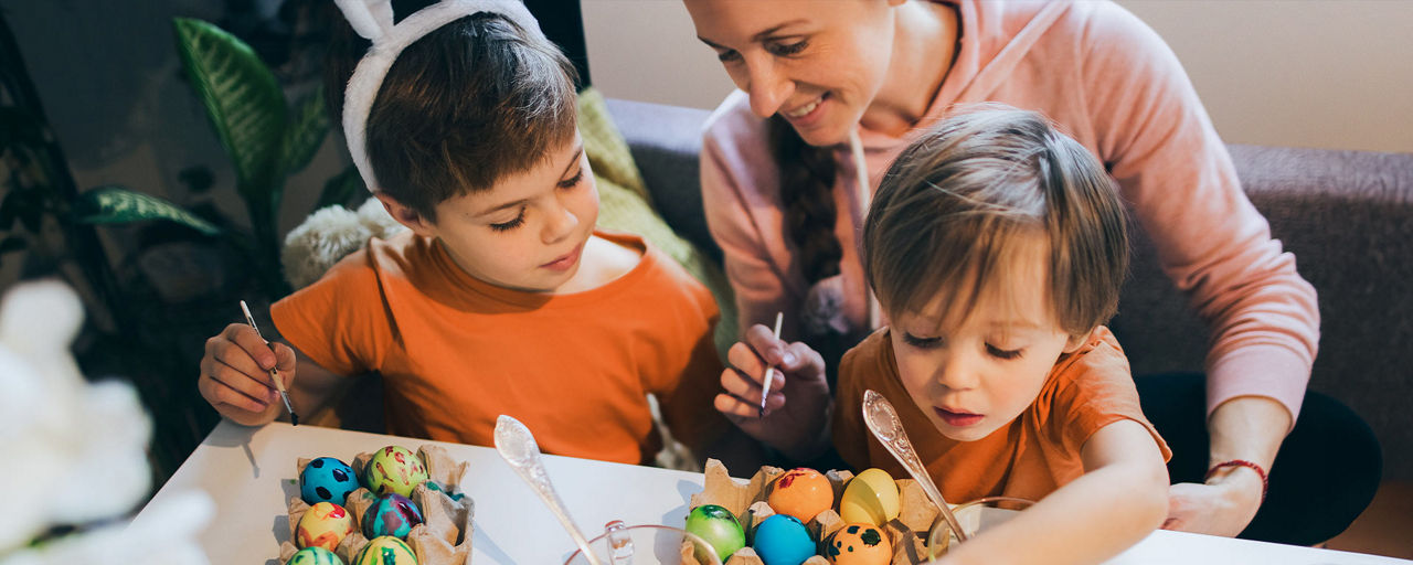 Eine Frau färbt mit zwei kleinen Kindern Ostereier.