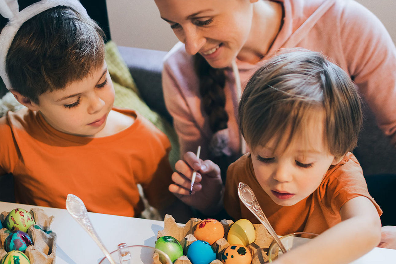 Eine Frau färbt mit zwei kleinen Kindern Ostereier.