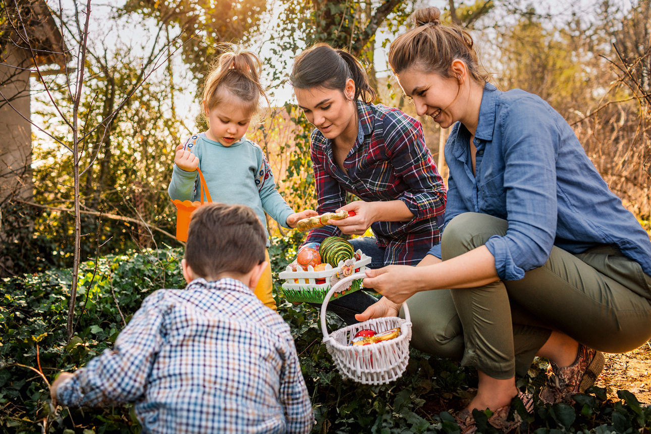 Zwei Kinder und zwei Frauen haben Osterkörbchen in der Hand und suchen im Garten nach Ostereinern