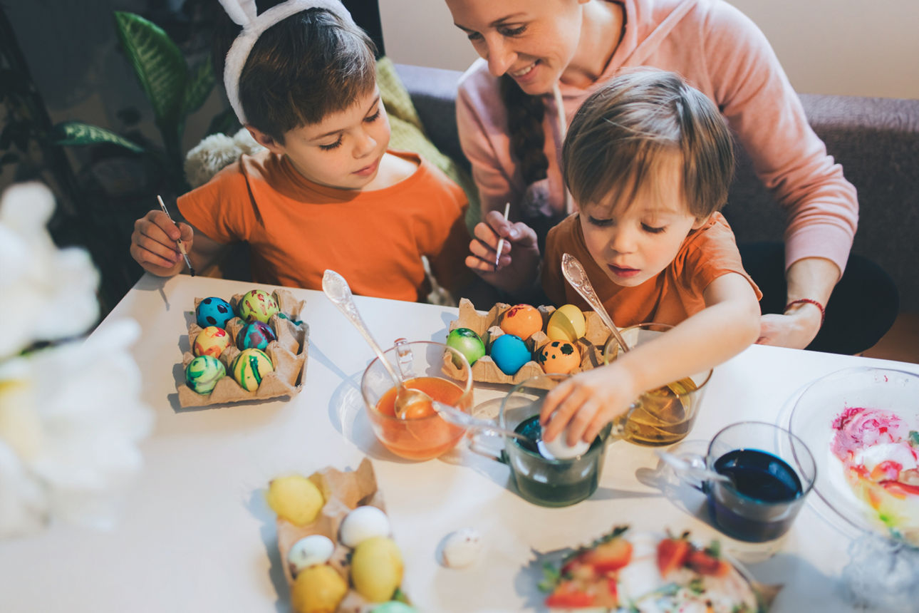 Zwei Kinder die mit Ihrer Mutter am Tisch Eier bemahlen