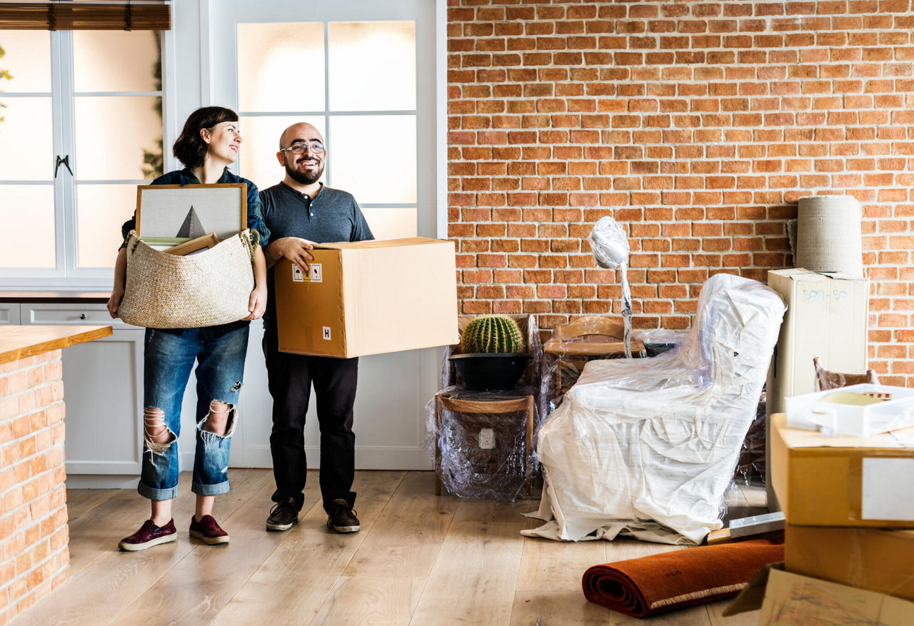 Ein Paar trägt Umzugskisten in die neue Wohnung und freut sich