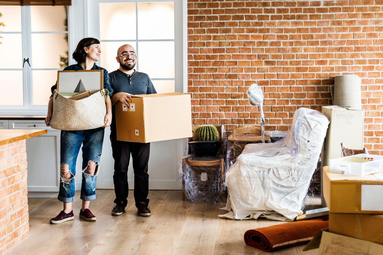Ein Paar trägt Umzugskisten in die neue Wohnung und freut sich