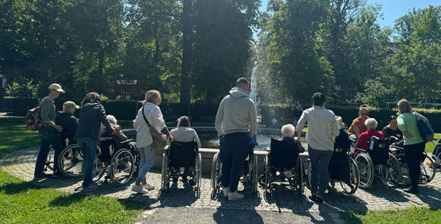 Mitarbeiter der PSD Bank Karlsruhe-Neustadt, die Senioren im Park in ihren Rollstühlen spazierenfahren.