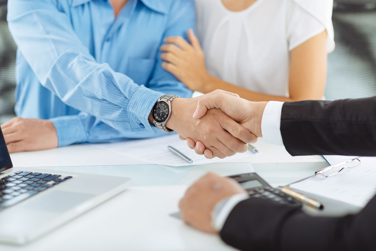 Ehepaar sitzt am Bürotisch. Mann reicht seine Hand dem gegenübersitzendem Hand zum Handshake