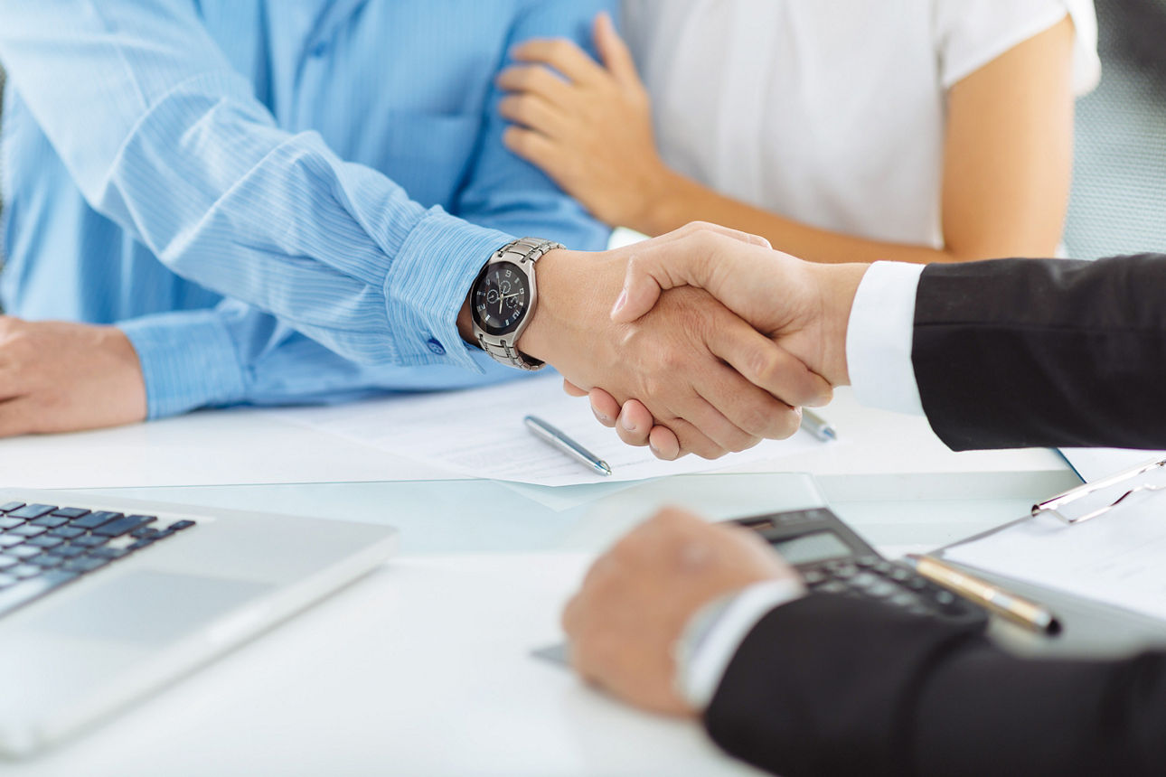Ehepaar sitzt am Bürotisch. Mann reicht seine Hand dem gegenübersitzendem Hand zum Handshake