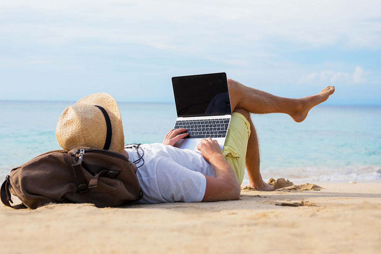 Mann liegt entspannt am Strand mit Laptop