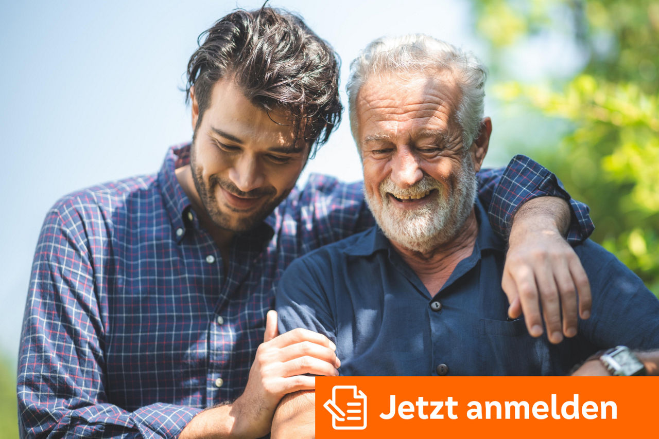 Zwei Personen sitzen eng beieinander im Grünen und legen fürsorglich die Arme umeinander.