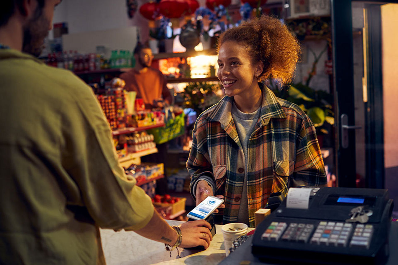 Eine june Frau zahlt an einer Ladenkasse mit der Pay App auf ihrem Smartphone
