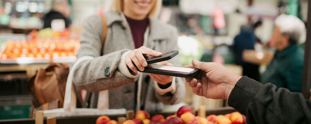 Eine junge Frau zahlt an einem Marktstand mit der App Digitales Bezahlen auf ihrem Android-Smartphone