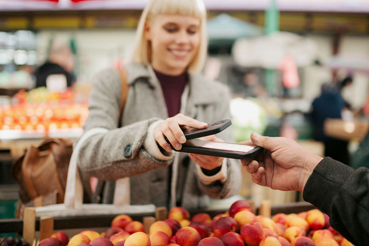 Eine junge Frau zahlt an einem Marktstand mit der Pay App auf ihrem Android-Smartphone