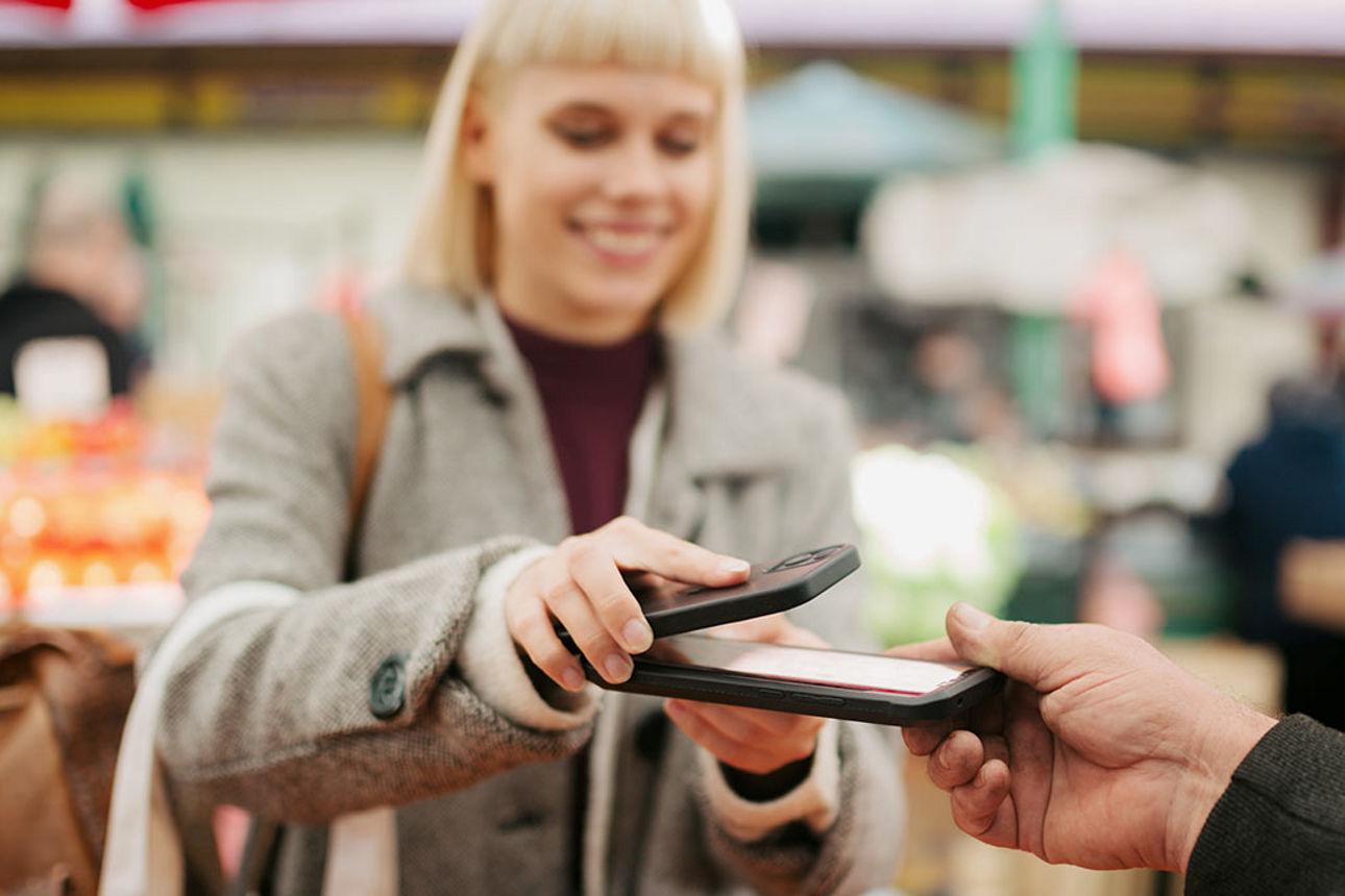Eine junge Frau zahlt an einem Marktstand mit der Pay App auf ihrem Android-Smartphone