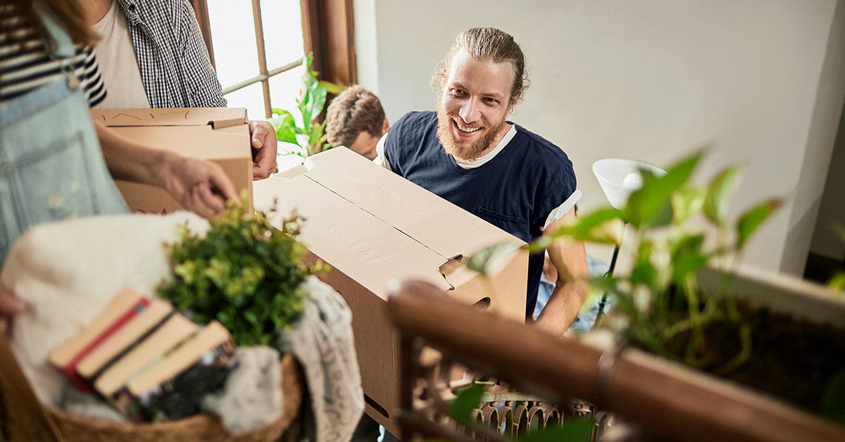 Erste eigene Wohnung - Ein junger Mann trägt eine gepackte Umzugskiste eine Treppe hoch