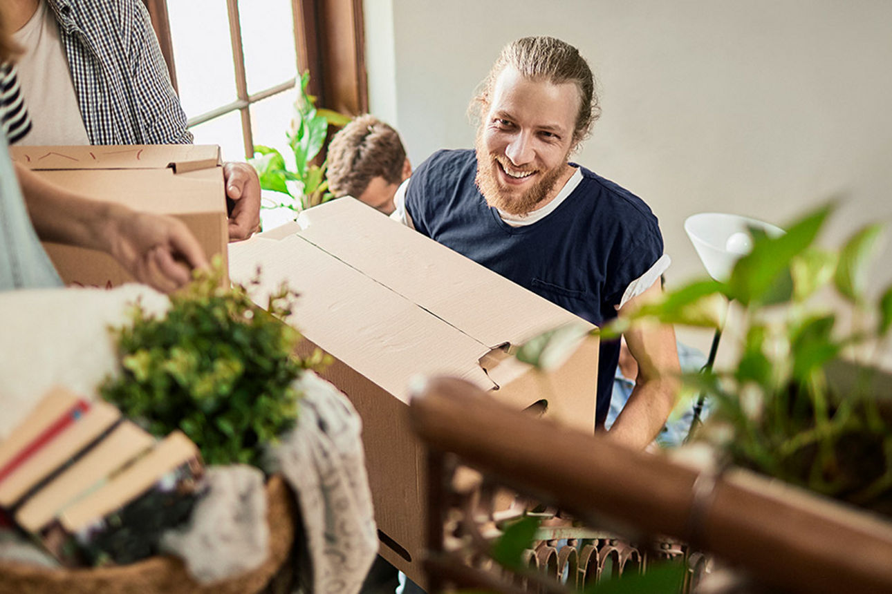 Ein junger Mann trägt eine gepackte Umzugskiste eine Treppe hoch