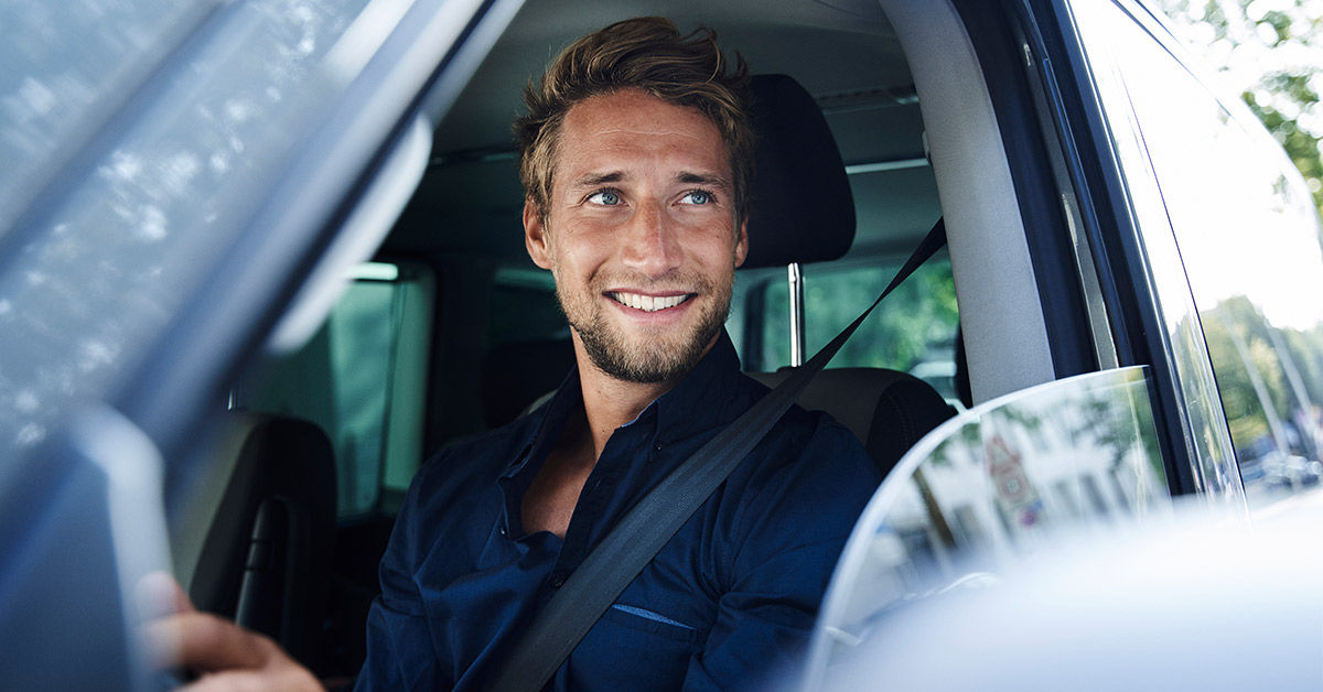 Führerschein und Auto - Junge Mann sitzt hinter dem Lenkrad eines Autos und lächelt durch das offene Fenster